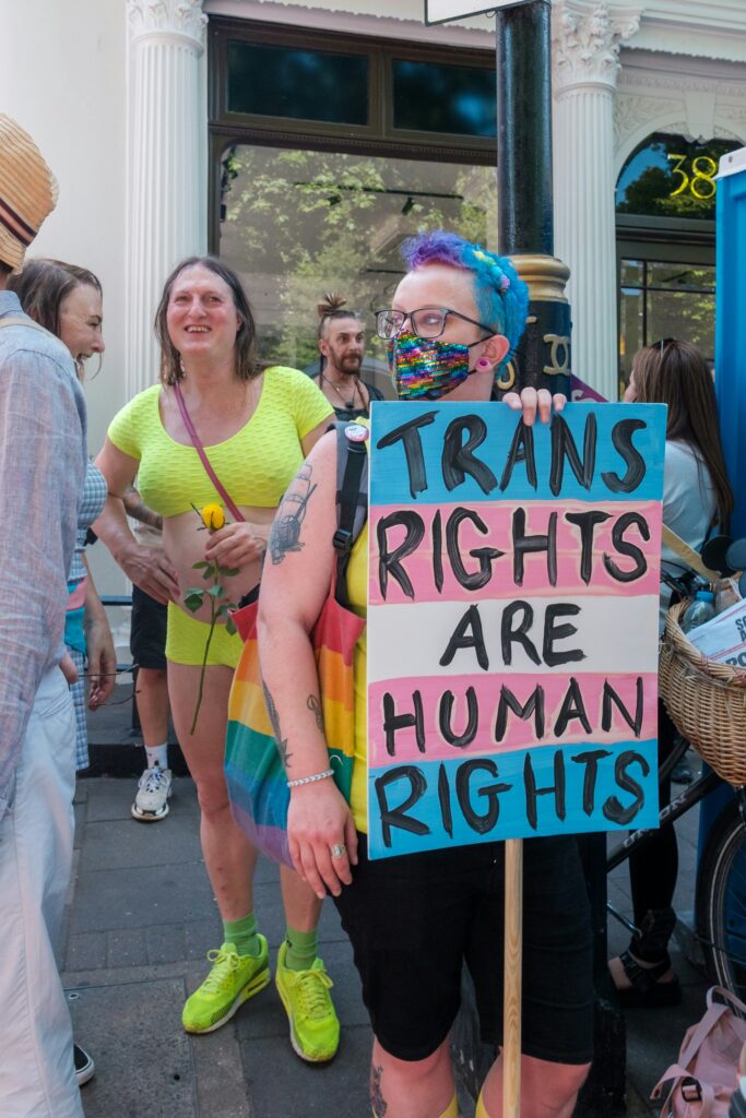 A person at some sort of rally or protest holding a sign with the colors scheme of the trans flag. The sign reads: "Trans rights are human rights" in all caps.