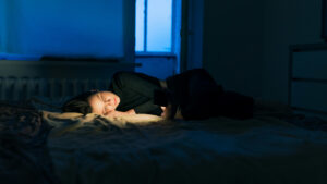 Woman staring at her phone screen on her bed with the lights turned off