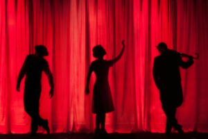Silhouettes of three people on stage with a red curtain behind