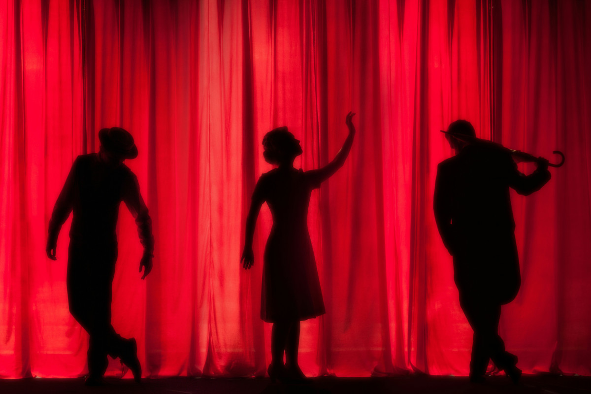 Silhouettes of three people on stage with a red curtain behind